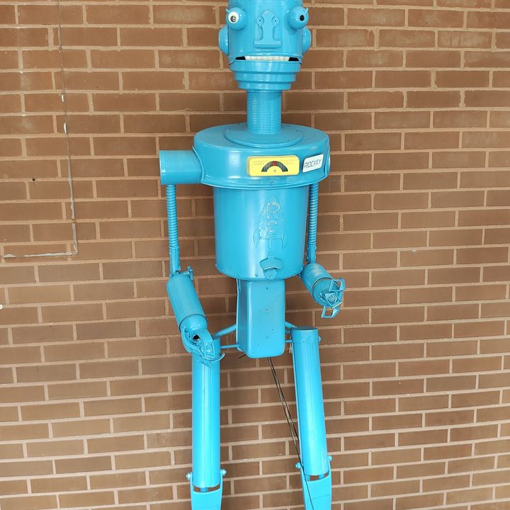 A blue robot standing against a brick wall, taken with the Motorola Razr Plus.