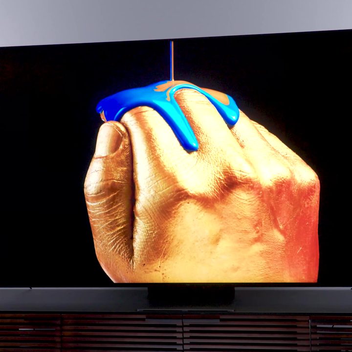 A stylized image of metallic blue paint being poured over hand shown on a a TCL QM8.