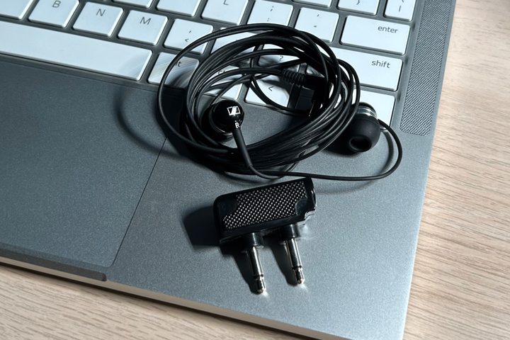 A set of Sennheiser wired earbuds seen with an airplane travel adapter, sitting on a laptop keyboard.