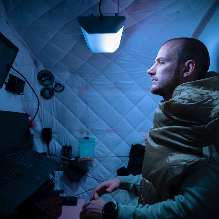 A man works in a small room with a Circadian Rhythm Light on a blue setting.