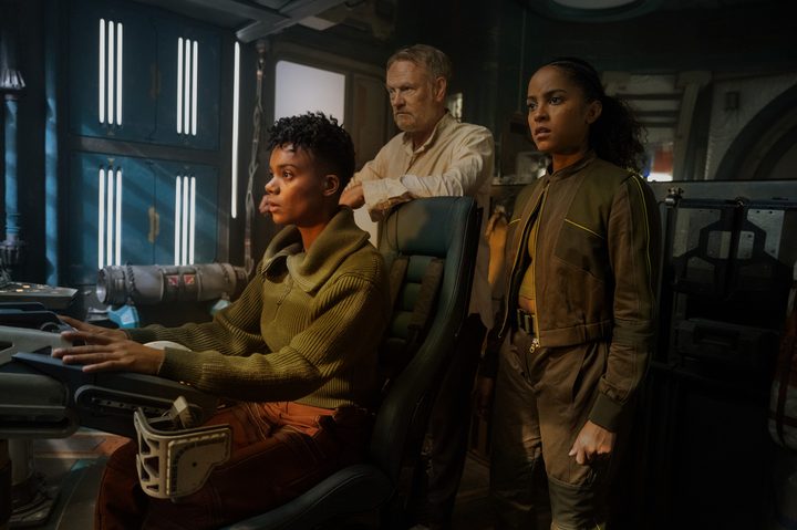 One character pilots a ship as two characters stand behind in Foundation.