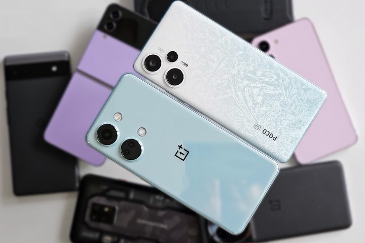White Xiaomi POCO F5 and bluish-green OnePlus Nord 3 held in hand over a heap of Android smartphones including OnePlus 11, Pixel 6a, Samsung Galaxy Z Flip 4, Galaxy S23.