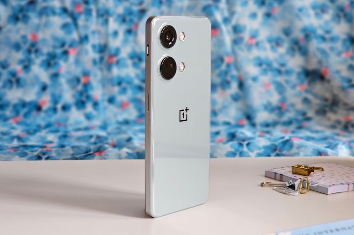 OnePlus Nord Misty Green color against a backdrop with white and blue flowers.