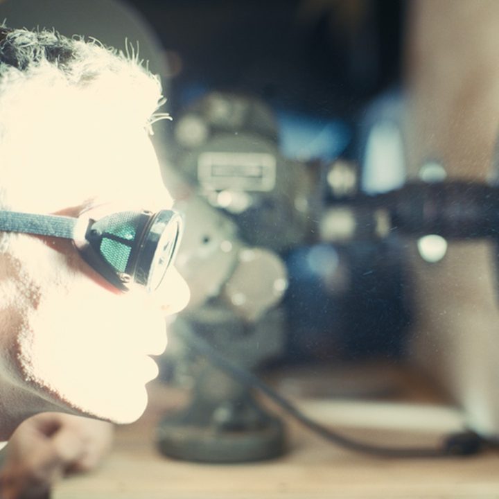 Cillian Murphy stares through a small window at an atomic blast, his face illuminated by light.