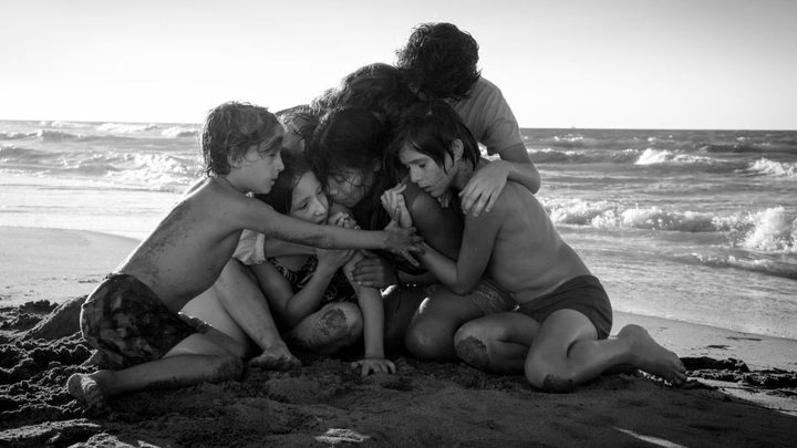 A group of children and two women embracing on the beach in the movie Roma.