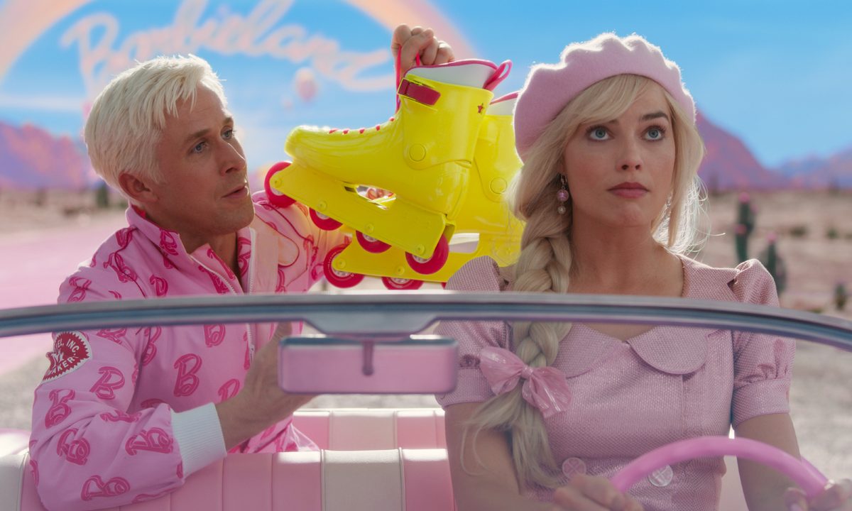 Ryan Gosling holds up a pair of rollerblades behind Margot Robbie in Barbie.