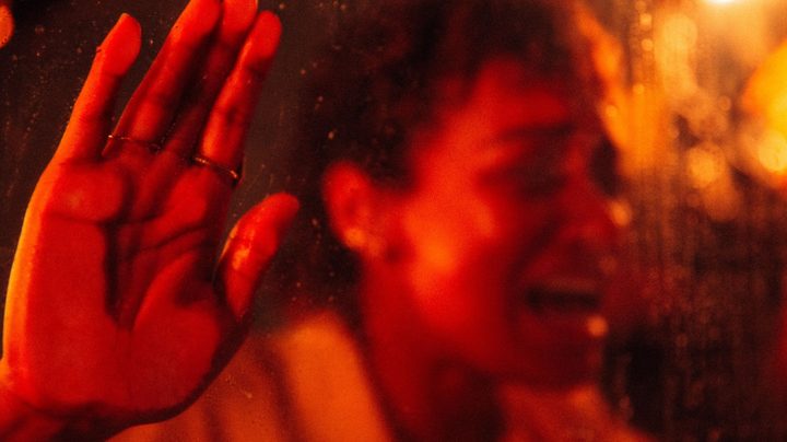Sophie Wilde bangs on a car window from the inside, bathed in red light.
