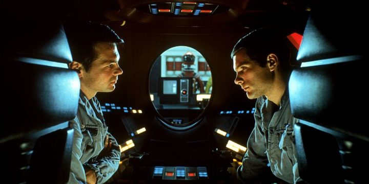 Two astronauts sit in a spaceship talking.