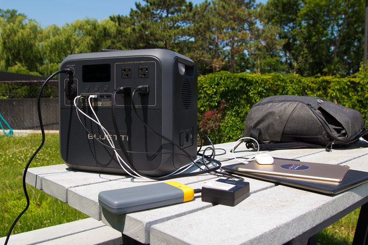 The Bluetti AC180 power station charging multiple devices simultaneously on a picnic table.