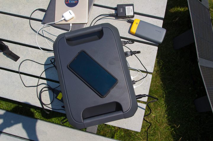 The Bluetti AC180 power station wirelessly charging a phone while charging other devices via cables.