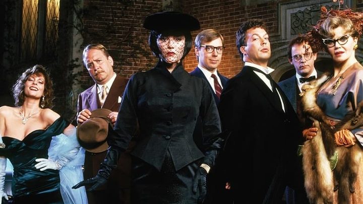 The cast of Clue pose in front of a mansion.