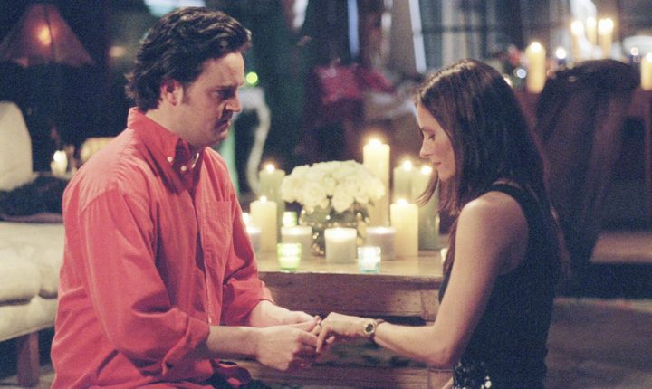 Chandler proposing to Monica while both are kneeling on the floor in a scene from Friends.