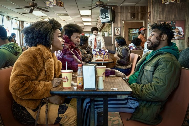 Three people sit at a table in They Cloned Tyrone.
