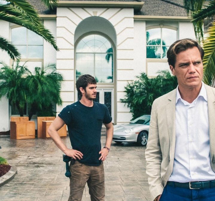 Andrew Garfield stands behind Michael Shannon in front of a house in 99 Homes.