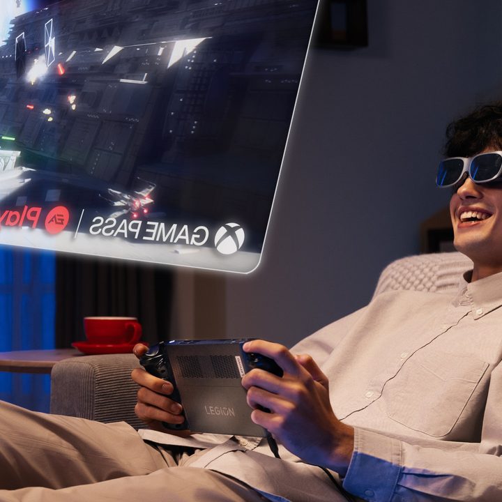 A closeup of a person reclining on a sofa, playing a game on Lenovo Legion Go while looking up at a virtual screen in Legion glasses.