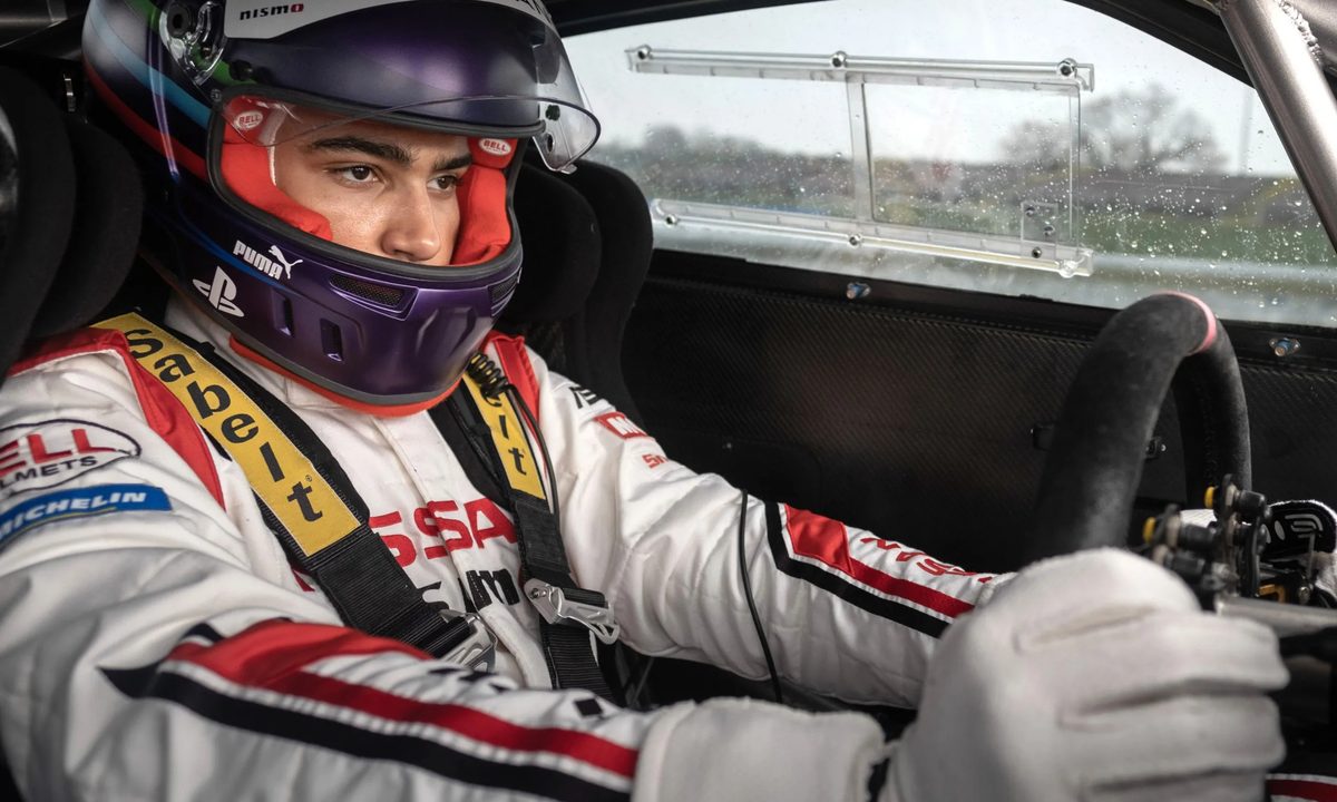 Archie Madekwe sits in a race car in Gran Turismo.