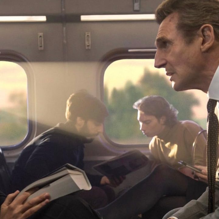 Two train passengers sit across from one another in The Commuter.
