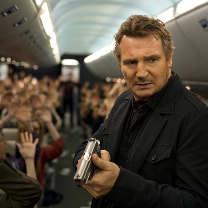 Liam Neeson wields a gun while standing in the aisle on a plane in Non-Stop.