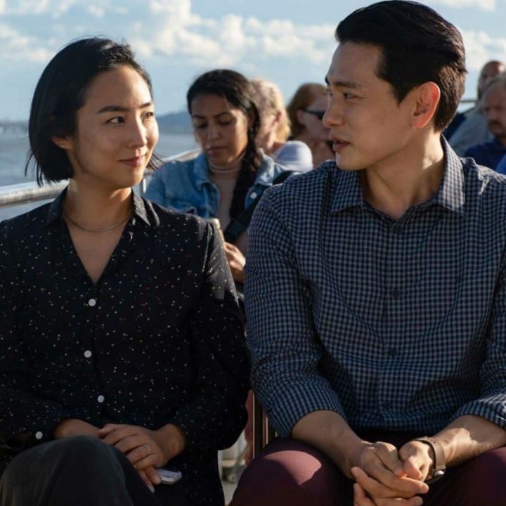 Two people sit next to each other on a boat and stare in Past Lives.