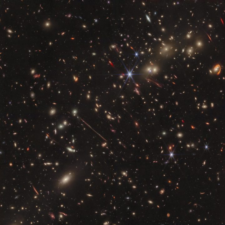 Webb’s infrared image of the galaxy cluster El Gordo (“the Fat One”) reveals hundreds of galaxies, some never before seen at this level of detail. El Gordo acts as a gravitational lens, distorting and magnifying the light from distant background galaxies. Two of the most prominent features in the image include the Thin One, located just below and left of the image center, and the Fishhook, a red swoosh at upper right. Both are lensed background galaxies.