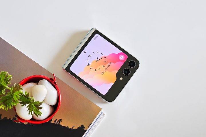 Samsung Galaxy Z Flip 5 lying on a flat surface with analog clock as cover screen wallpaper.
