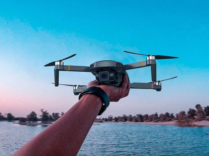 A hand holding a drone in front of a lake.