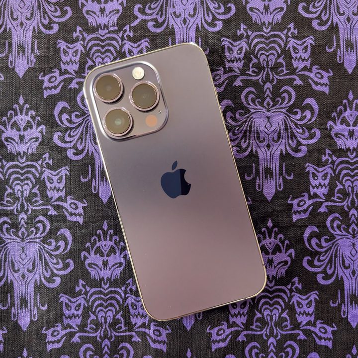 A Deep Purple iPhone 14 Pro on top of a Haunted Mansion wallpaper placemat.