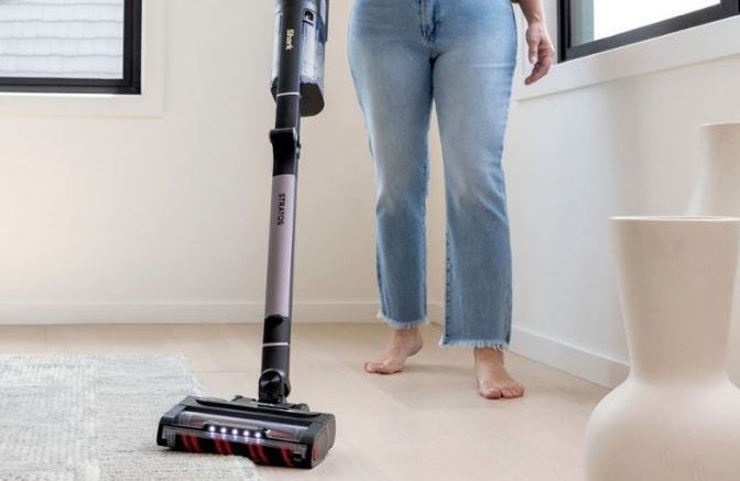 A woman using the Shark Stratos MultiFLEX vacuum on a white carpet.