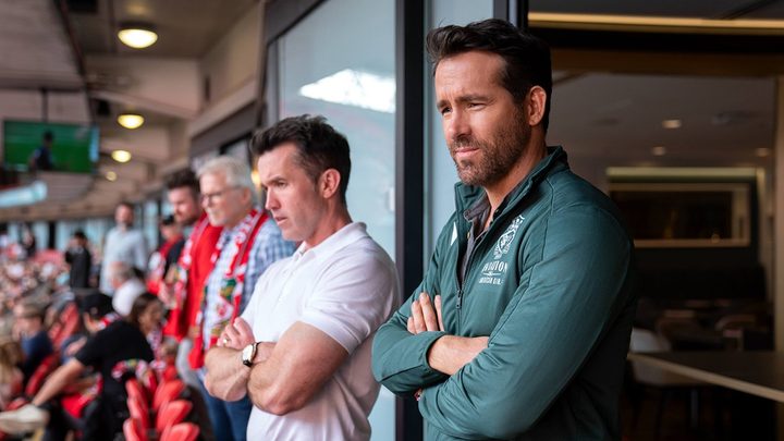 Rob McElheny and Ryan Reynolds stand to watch a football game in a scene from Welcome to Wrexham