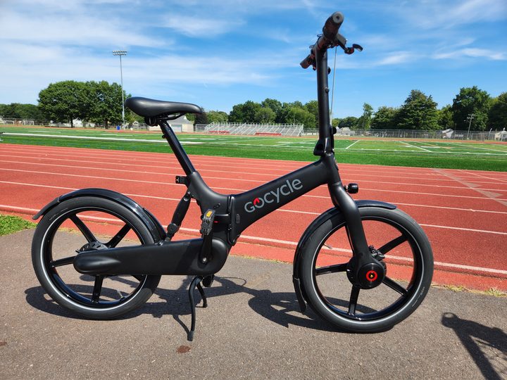 A GoCycle G4 folding e-bike parked next to a football field.