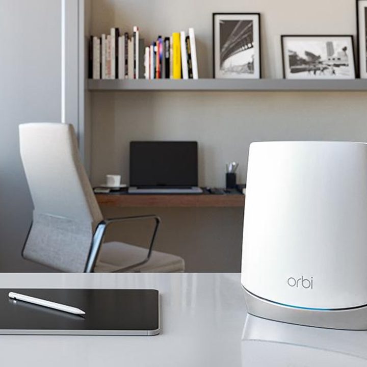 Netgear's Orbi CBR750 sits on a table beside an iPad, with a laptop is in the background.
