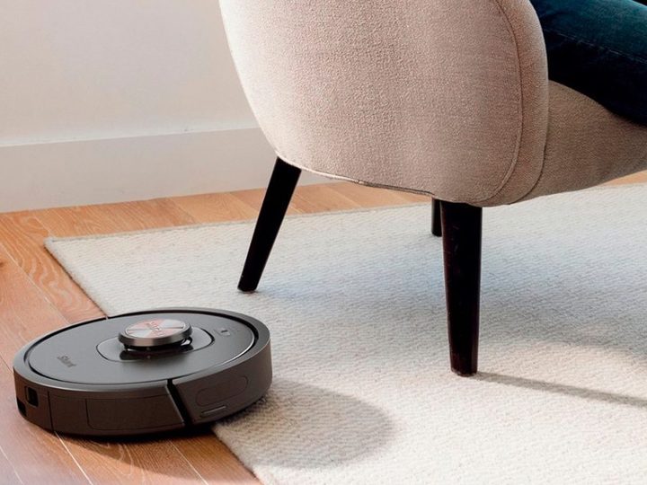The Shark Matrix robot vacuum cleaning a rug while a person reads in a chair.