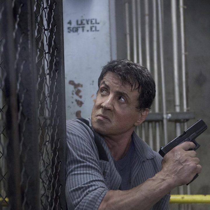Sylvester Stallone holding a gun on a fence in Escape Plan.