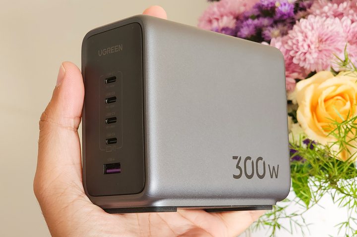 Ugreen 300W GaN fast charger with four USB-C and one USB-A port in hand held against pink and yellow flowers.