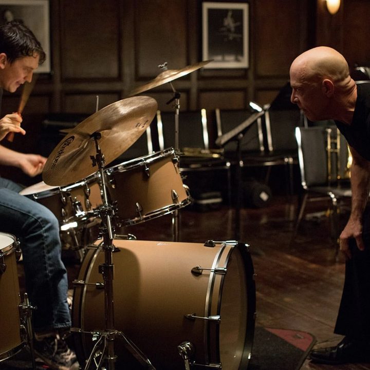 Miles Teller drums while JK Simmons stares in front in Whiplash.