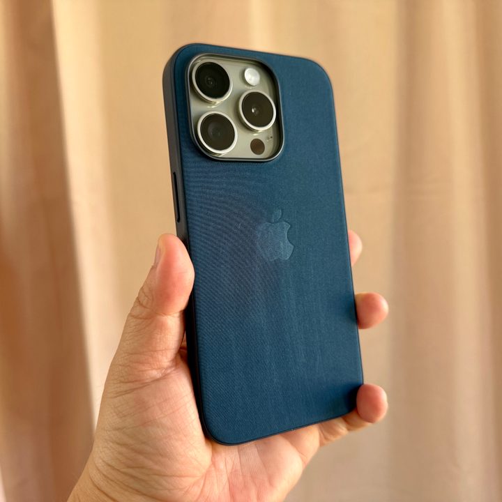 Natural Titanium iPhone 15 Pro in Pacific Blue FineWoven case held in hand showing wear and tear.