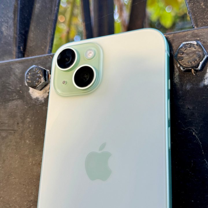 A green iPhone 15 showing the camera and matte glass back.
