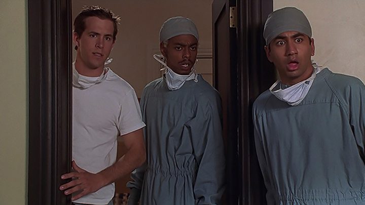 Ryan Reynolds in a white T-shirt with two men dressed as doctors in a scene from National Lampoon's Van Wilder.