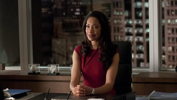Jessica from Suits sitting at her desk, hands clasped in front of her.