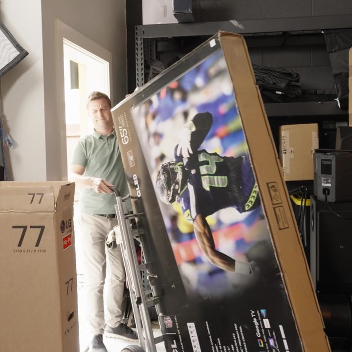 A man navigates a boxed TV into a storage space using a hand truck.