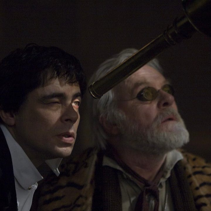 A man looks through a telescope while standing next to someone else in The Wolfman.