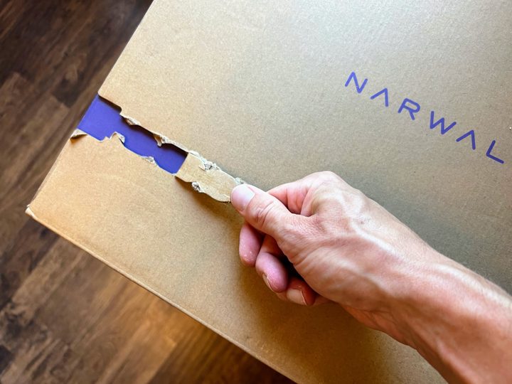 A hand pulls the opening tab on the packaging for the Narwal Freo robot vacuum and mop.
