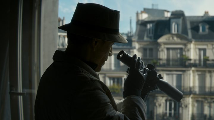 Michael Fassbender looks through a scope and out a window.