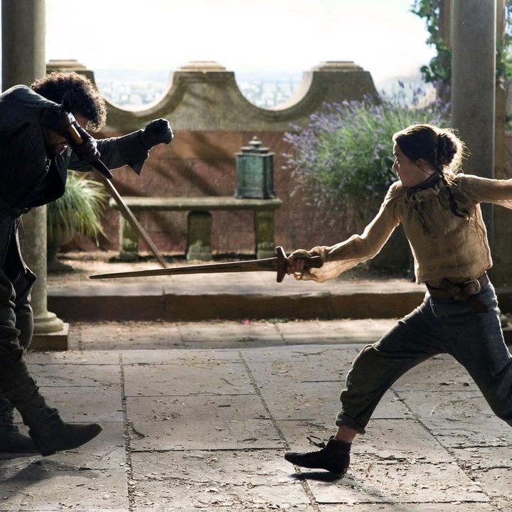 A man and young girl spar with swords.