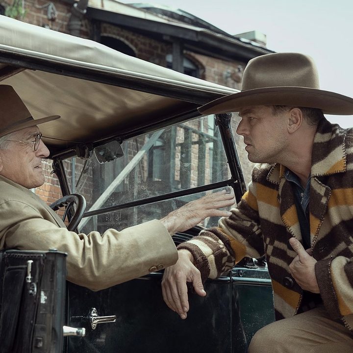 A man leans up against a car while another man holds his arm in Killers of the Flower Moon.