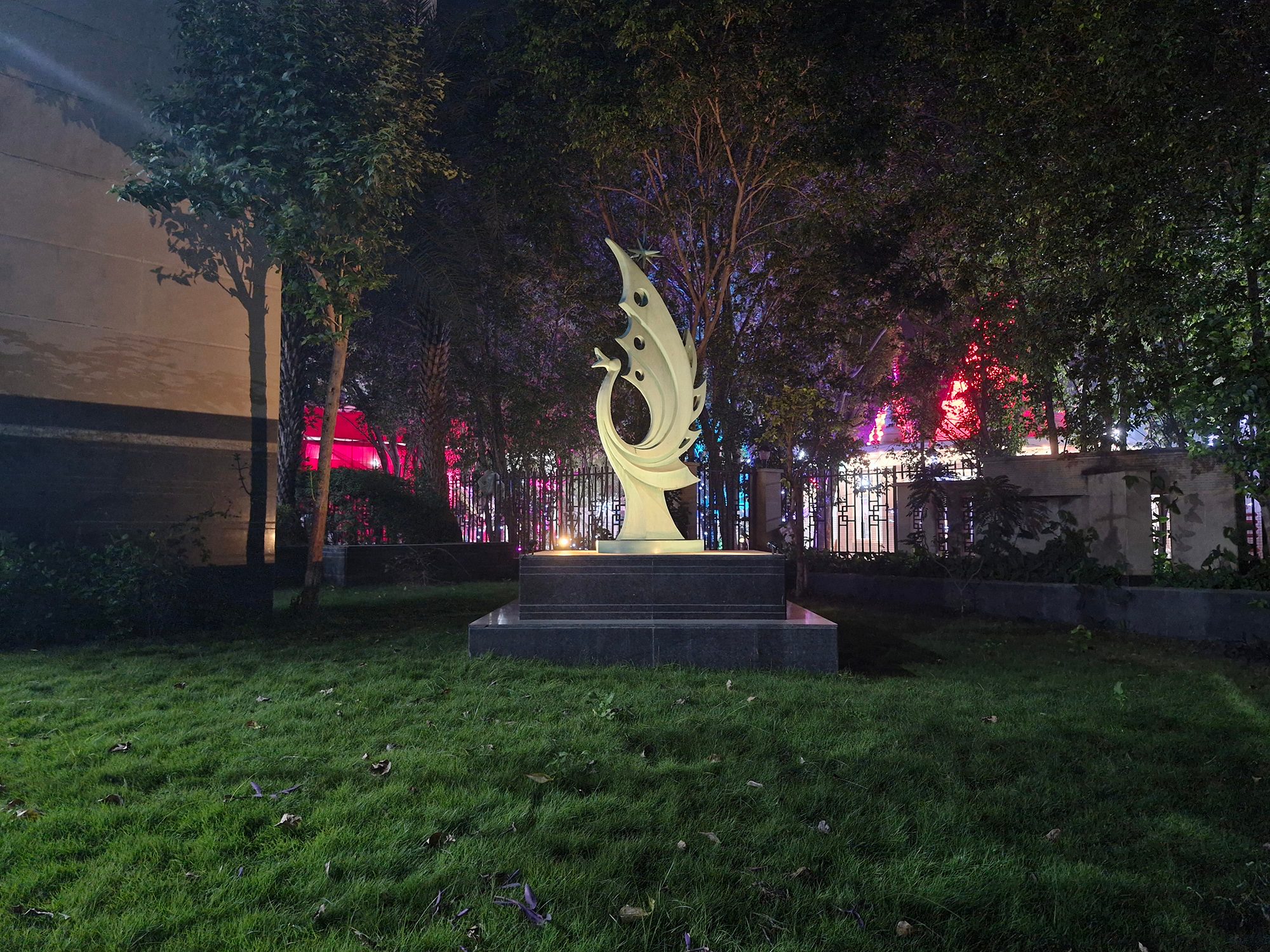 Green sculpture on a marble platform over grass photographed with the Samsung Galaxy S23 FE at night.