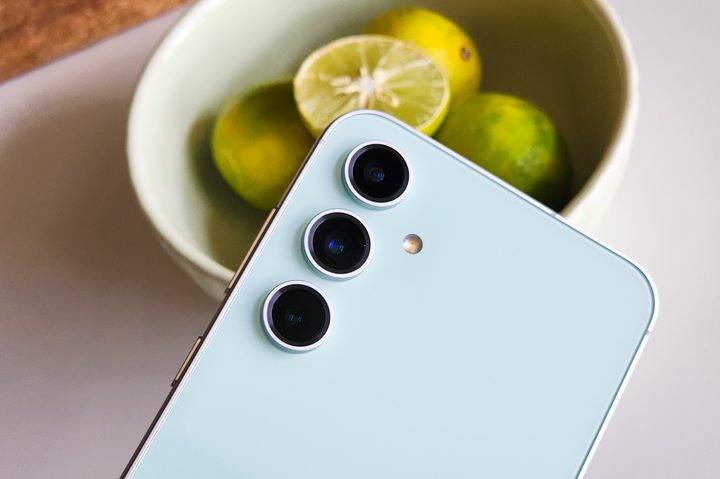 Rear camera setup on the Samsung Galaxy S23 FE Mint Green held in front of a bowl of lemons.