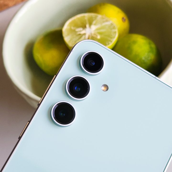 Rear camera setup on the Samsung Galaxy S23 FE Mint Green held in front of a bowl of lemons.
