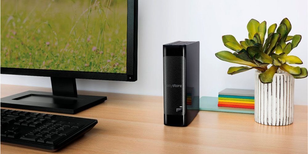 The WD Easystore 14TB External USB 3.0 hard drive on a desk next to a monitor and near a plant.