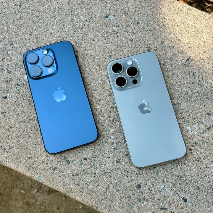 Blue Titanium (left) and Natural Titanium iPhone 15 Pros on a concrete bench.
